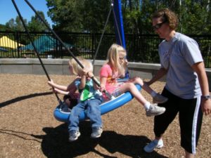 Mom pushing three kids on swing at Elm Creek Play Area