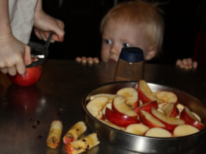 Child slicing apples while a toddler looks on