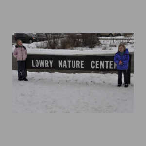 Two girls standing by Lowry Nature Center sign in the winter