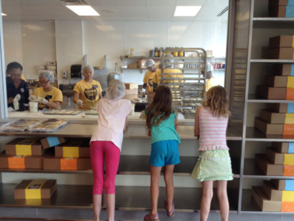 Three girls watch as cookie cart bakers make cookies