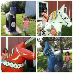 Collage of little girl posing next to four giant Dala horses around the grounds of Gammelgården of Scandia, Minnesota