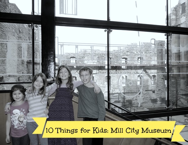 Four kids with arms around each other standing in front of the window to the Mill Ruins Courtyard at the Mill City Museum in Minneapolis, MN