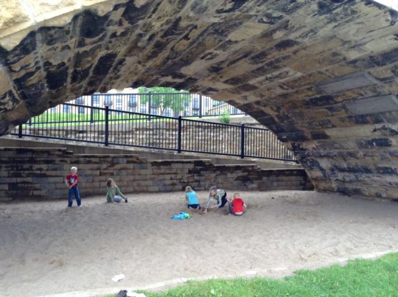 Kids playing in the "Stone Arch Sandbox" sandy area below the Stone Arch Bridge in Minneapolis, Minnesota