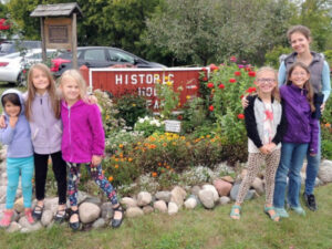Girls and woman standing in front of the Historic Holz Farm sign and garden, Eagan, Minnesota