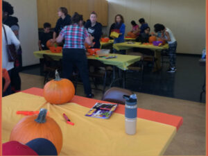 Families carving pumpkins in the Multipurpose Room in Bottineau Field Park Rec Center in Minneapolis, Minnesota