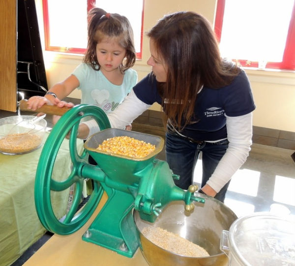 Three Rivers Parks staff showing little girl how to grind corn into meal at Gale Woods Farm in Minnetrista, MN