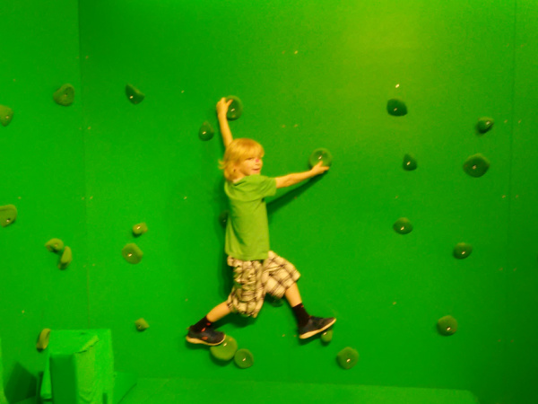 Boy climbing along green screen climbing wall in the Super Awesome Adventures exhibit at the Minnesota Children's Museum in St. Paul, MN
