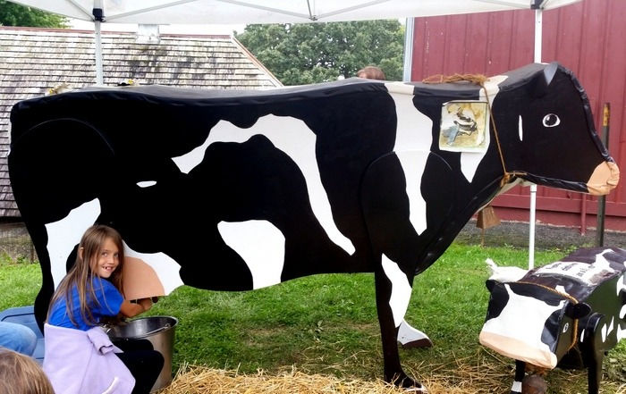 Girl trying out "milking" a wood cutout cow at Holz Farm Park in Eagan Minnesota