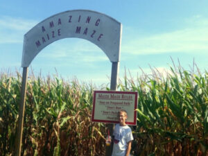 Boy standing in front of entrance to corn maze at Croix Farm Orchard in Hasting Minnesota. Sign Reads "Maize Maze Rules: 'Stay on Prepared Path' 'Don't Run' 'Don't Pick' Thank You"