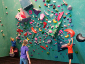 Three kids climbing a colorful wall at the Minneapolis Bouldering Project