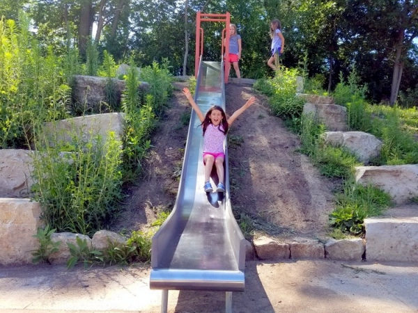 Girls sliding down slide in the Frogtown Farm Park nature playground - St. Paul, Minnesota