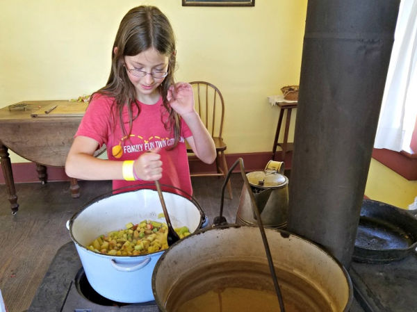 Girl stirring a stew cooking on a wood stove at the Oliver Kelley Farm in Elk River, Minnesota