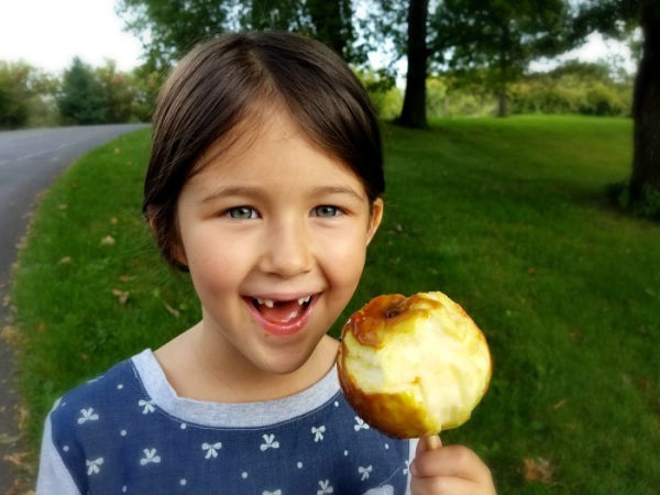 Girl with two top front teeth missing eating a caramel apple at Sunrise River Farm in Wyoming, Minnesota