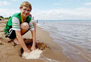 Boy digging a hole for water to pool in the sand on the shores of Lake Superior at Park Point Beach in Duluth, Minnesota.