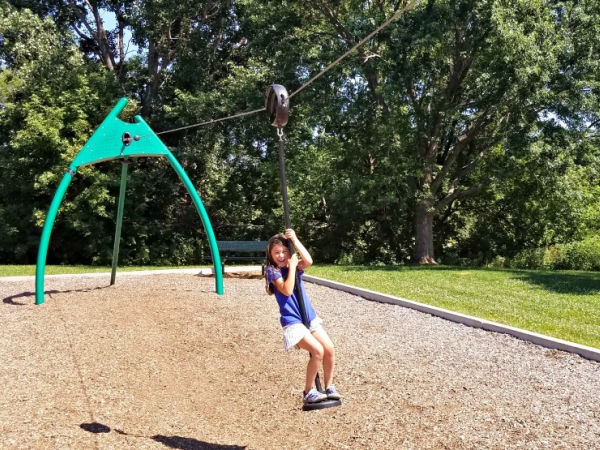 Girl riding the playground zipline at Veterans Memorial Park in Richfield, Minnesota