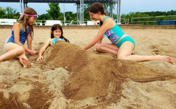 Girl burying another girl in sand at Wirth Lake Beach in Minneapolis, Minnesota