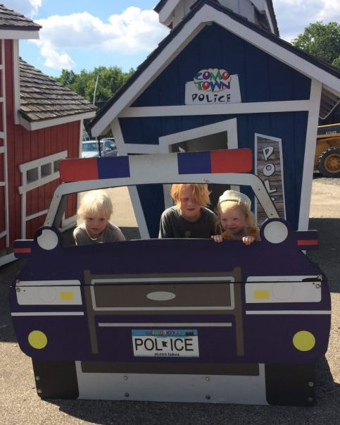 Three kids posing in a cut out of a police car at Como Town Amusement Park in Saint Paul Minnesota