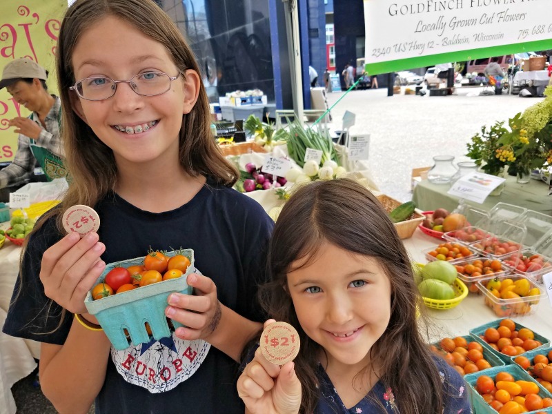 Girls showing their $2 wooden coins at a fall farmers market