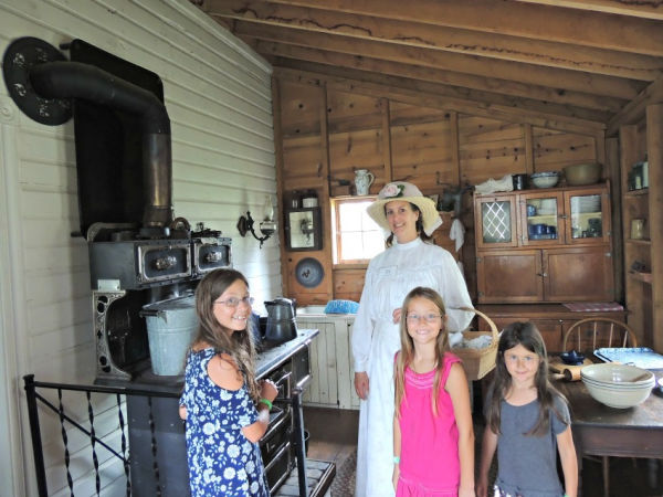 Girls and costumed guide in kitchen of Dakota City Heritage Village in Farmington Minnesota