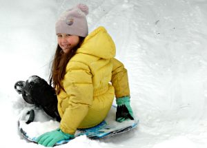 Girl in a yellow parka and pink hat sledding.