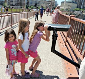 Three girls looking through a view scope on the Stone Arch Bridge in Minneapolis, Minnesota.