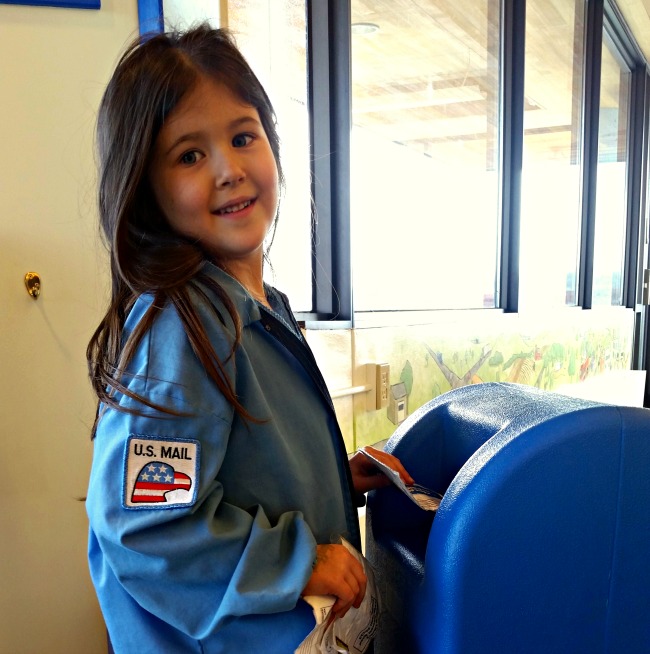 Girl playing mail carrier with dress up uniform and toy mailbox at Wescott Library in Eagan Minnesota