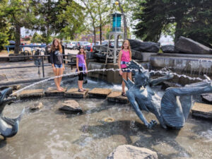 Three girls crossing stepping stones by the Fountain of the Wind in Canal Park in Duluth, Minnesota.