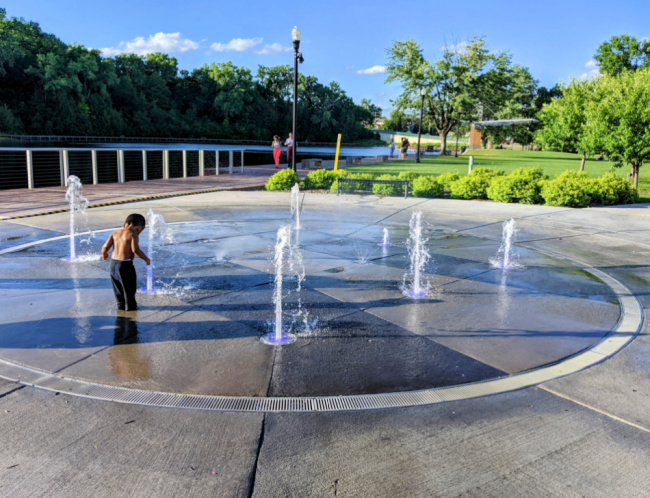 Toddler boy splashing in fountain style splash pad at Clayhole Park in Chaska, Minnesota
