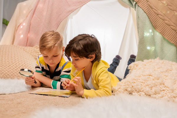 Two boys studying a map in a blanket tent