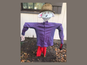 Scarecrow with straw hat, anime face, purple shirt and red pants.