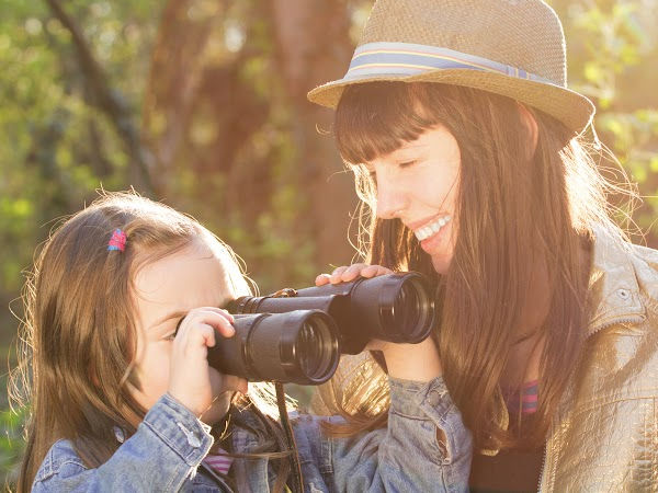 Little girl looking through binoculars as mother helps