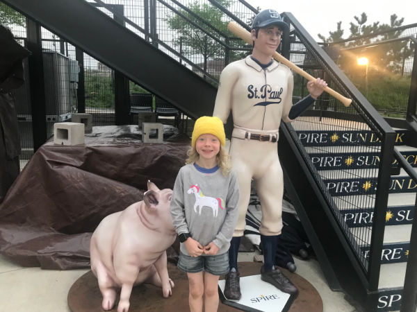 Girl standing by sculpture of St. Paul Saints Player and pink pig