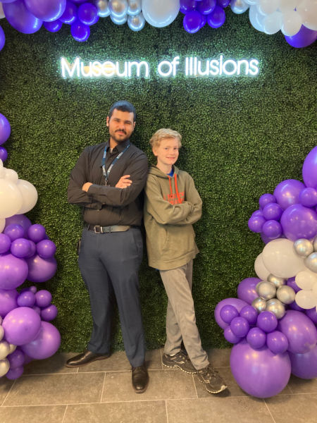 two young men posing under museum of illusions sign with purple and white balloons