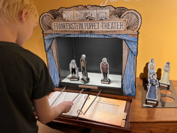Boy playing with a puppet theater in the Mary & Her Monster Exhibit at Bakken Museum, Minneapolis, MN